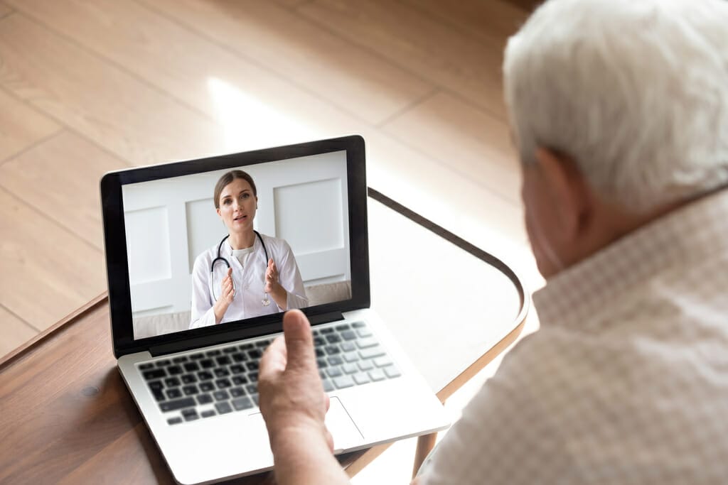 Close up older man talking with doctor by video call, using medical apps on laptop, service, friendly young woman wearing white uniform coat with stethoscope consulting mature senior patient online